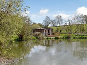 Eine Holzhütte mit einer Terrasse, umgeben von einem Teich und Bäumen.