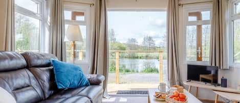 A room with a leather sofa, a TV, a table with snacks, and a view of a lake.