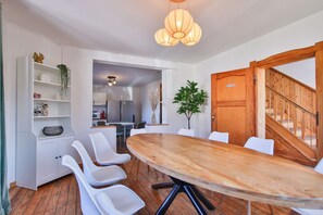A modern dining area with a wooden table, white chairs, and a hanging light fixture. - L'Ecureuil Vacation Rental - Maisons Paladins (Malmedy)