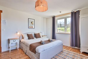 Een slaapkamer met een bed, nachtkastjes, een hanglamp, een raam met gordijnen en uitzicht op het buiten.