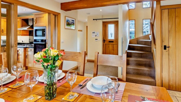 A dining area with a wooden table set for four, a kitchen in the background, and a wooden staircase. - 4 Bed in Ambleside (oc-83055) (Ambleside)