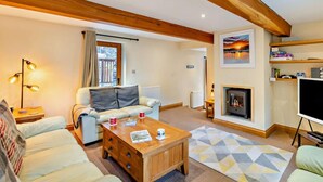 A living room with a sofa, coffee table, fireplace, TV, and wooden ceiling beams. - 4 Bed in Ambleside (oc-83055) (Ambleside)