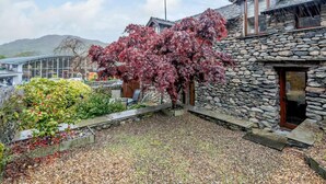 A stone building with a wooden door, a tree with red leaves, and a gravel driveway. - 4 Bed in Ambleside (oc-83055) (Ambleside)