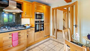 A modern kitchen with wooden cabinets, a gas stove, an oven, and a microwave. - 4 Bed in Ambleside (oc-83055) (Ambleside)