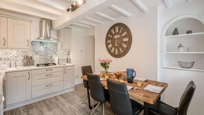 Eine moderne Küche mit weißen Schränken, einer großen Uhr und einem Essbereich mit Holztisch und Stühlen.