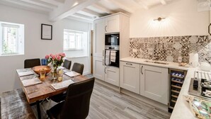 Eine moderne Küche mit weißen Schränken, einer gemusterten Spritzschutzwand und einem Essbereich mit Holztisch und Stühlen.