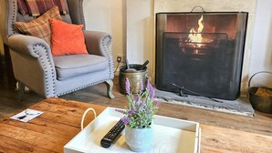 Ein Wohnzimmer mit grauem Sessel, Kamin, Couchtisch aus Holz und Fernbedienung.