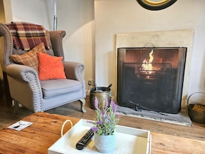 Ein Wohnzimmer mit grauem Sessel, Kamin, Couchtisch aus Holz und Fernbedienung.