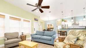 A living room with a ceiling fan, a sofa, a coffee table, and a patterned armchair. - Pet Friendly Retreat - Outdoor Living - Sleeps 9 - Sunset Patios (Port Aransas)