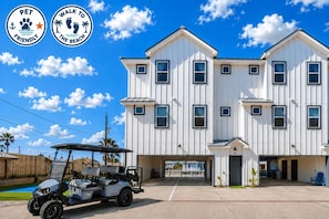 A two-story building with a white exterior, multiple windows, and a gated entrance. - Rooftop Ocean Views - Pool - Pickleball - Elevator - Golf Cart (Port Aransas)