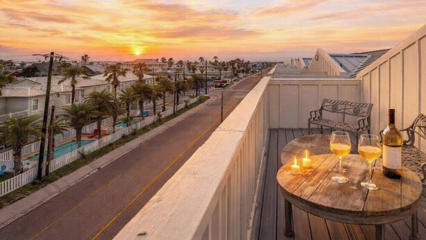 Un balcon avec une table, deux verres de vin et une bouteille de vin.