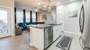 Une cuisine moderne dotée d’un îlot central, d’appareils électroménagers en acier inoxydable, de luminaires suspendus et offrant une vue sur la ville grâce à de grandes fenêtres.