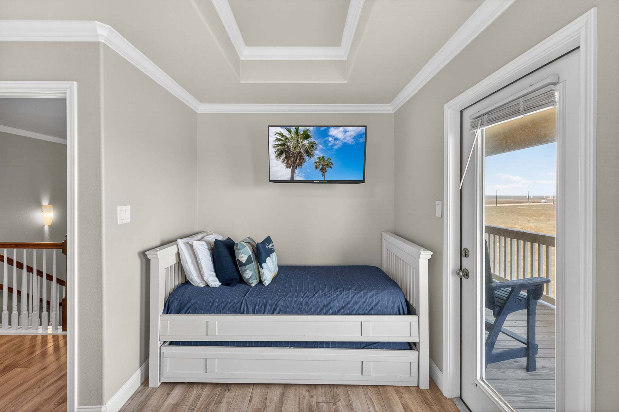Ein Schlafzimmer mit einem Bett, einem an der Wand befestigten Fernseher und einer Tür, die auf einen Balkon führt.