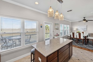 A kitchen with a large island, pendant lights, a dining area, and a view through the windows. - Your 4 Bedroom Coastal Escape! Ocean Views and Pet Friendly! (Port Aransas)