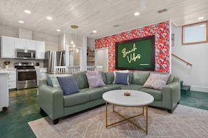 A modern kitchen with white cabinets, stainless steel appliances, and a green leather sofa with a round coffee table. - Old Town Oasis Rooftop Deck - Pool - Walk to Everything! (Port Aransas)