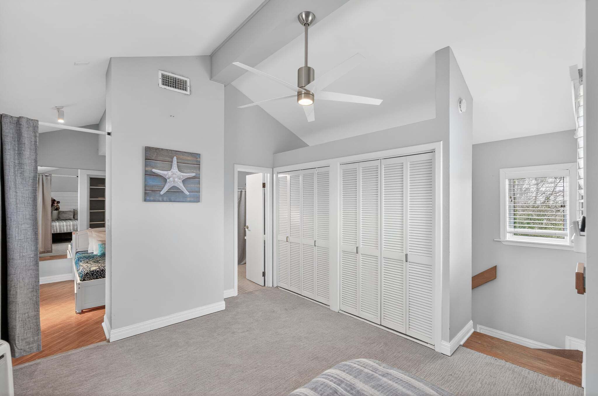 A spacious room with a ceiling fan, white closet doors, and a starfish decoration.
