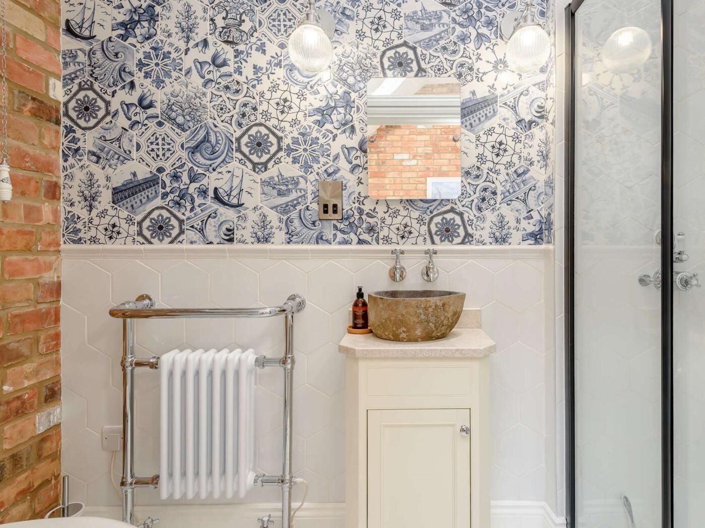 A bathroom with a tiled backsplash, a white cabinet, a large vessel sink, a towel rack, and a glass shower enclosure.
