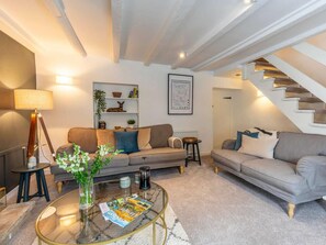 Ein Wohnzimmer mit Sofa, Couchtisch, Lampe, Bücherregal und einer Treppe.