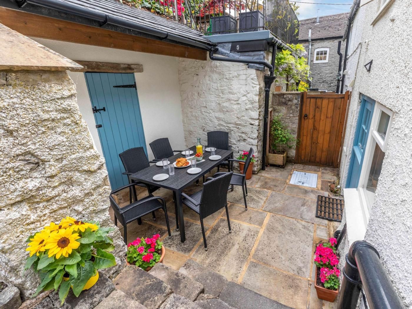 A stone patio with a table set for two, surrounded by potted plants and flowers.