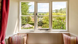 Ein Zimmer mit großem Fenster, einer gepolsterten Bank und Blick auf einen Garten.