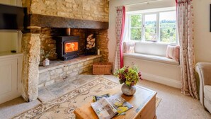Ein gemütliches Wohnzimmer mit Kamin aus Stein, einer bequemen Couch, einem Couchtisch mit Zeitschriften und einem Fenster mit Vorhängen.