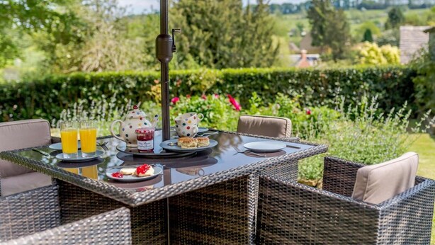 Ein Essbereich im Freien mit Korbmöbeln, einem Tisch für zwei Personen und Blick auf einen Garten.