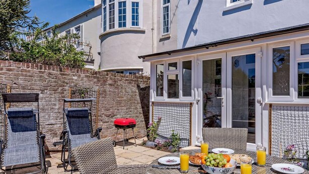 Eine Terrasse mit Korbmöbeln, einem Tisch mit Tellern, Gläsern und einer Obstschale.