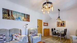 Ein Wohnzimmer mit Sofa, Sessel, Couchtisch, Esstisch, Stühlen und Kunstwerken an den Wänden.