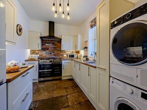 A compact kitchen with a built-in oven, microwave, and a front-loading washing machine. - 3 Bed in Bognor Regis (oc-83115) (Bognor Regis)