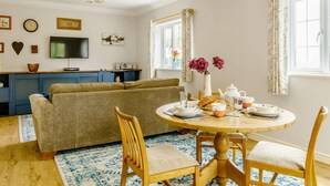 Ett mysigt vardagsrum med en soffa, ett matbord för två personer och en köksdel med en TV och blå skåp.