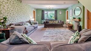 Ein Wohnzimmer mit zwei Sofas, einem Couchtisch, Wandtapete mit Muster, einem Deckenventilator und einem Fenster mit Vorhängen.