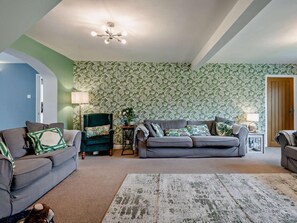 Ein Wohnzimmer mit grauem Sofa, einem grünen Sessel, raumakzentuierten Tapeten und einer Deckenleuchte.