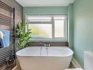 A bathroom with a freestanding bathtub, a window with patterned curtains, a towel rack with a blue towel, and a potted plant. - 5 Bed in Wareham (oc-83036) (West Lulworth)