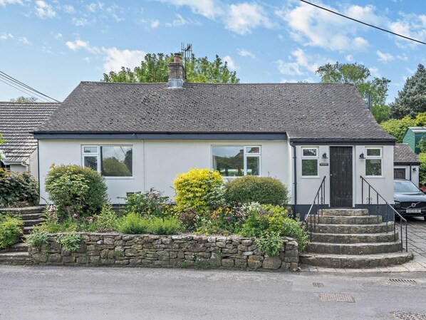 A single-story house with a stone foundation, a tiled roof, and a front garden with various plants and flowers. - 5 Bed in Wareham (oc-83036) (West Lulworth)