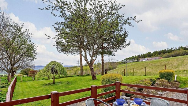 Terraza con mesa lista para comer, con vista a un paisaje cubierto de pasto, árboles y casas a lo lejos.