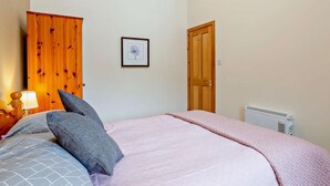 Un dormitorio con cama, mesita de noche, cuadro enmarco, puerta de madera y radiador.