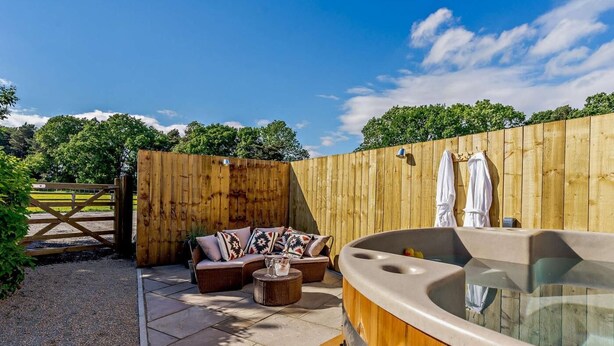 Een houten omheining, een jacuzzi en buitenmeubels met kussens.