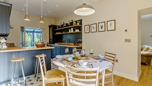 Een moderne keuken met een centraal eiland, hanglampen en een eethoek met een ronde tafel en stoelen.