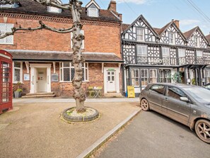 Ein traditioneller britischer Pub mit einer Fassade im Tudor-Stil, einer roten Telefonzelle und einem parkenden Auto auf der Straße.