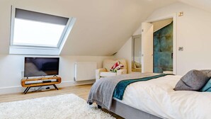Ein Schlafzimmer mit Oberlicht, Fernseher, Bett, Stuhl und Heizkörper.