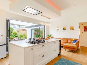 A modern kitchen with a central island, a dining area with a view, and a cozy living space with a sofa and cushions. - 4 Bed in Newquay (oc-83117) (Newquay)