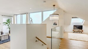 Ein großzügiges Loft mit hohen Decken, großen Fenstern, einer Treppe mit Glastrennstäben und einer Kronleuchter.