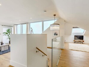 A spacious loft with a high ceiling, large windows, a staircase with glass railings, and a chandelier. - 4 Bed in Newquay (oc-83117) (Newquay)