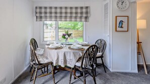 Un coin repas avec une table dressée pour quatre personnes, une horloge au mur et une fenêtre donnant sur l’extérieur.