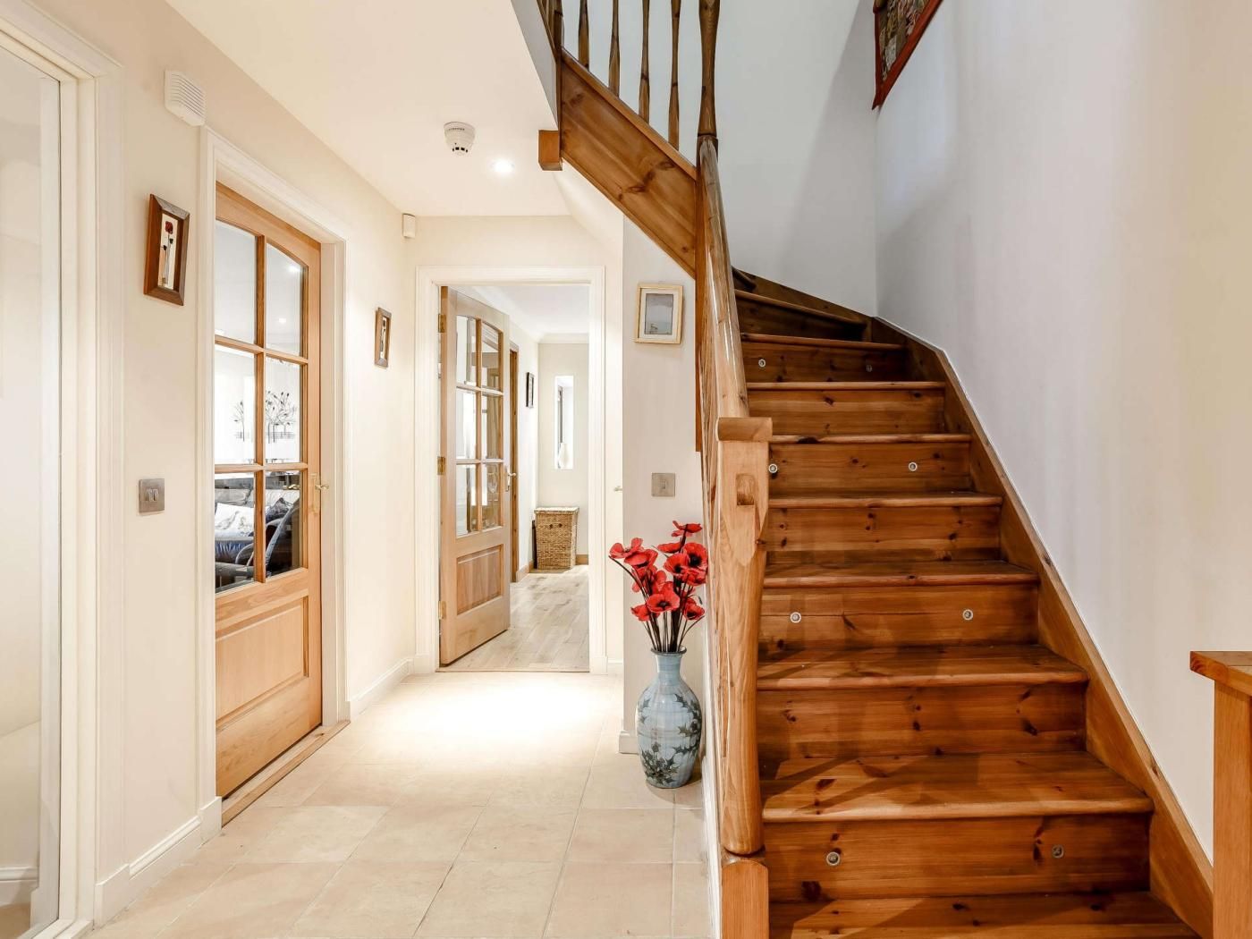 A wooden staircase with a handrail, leading to a landing with a vase of red flowers.