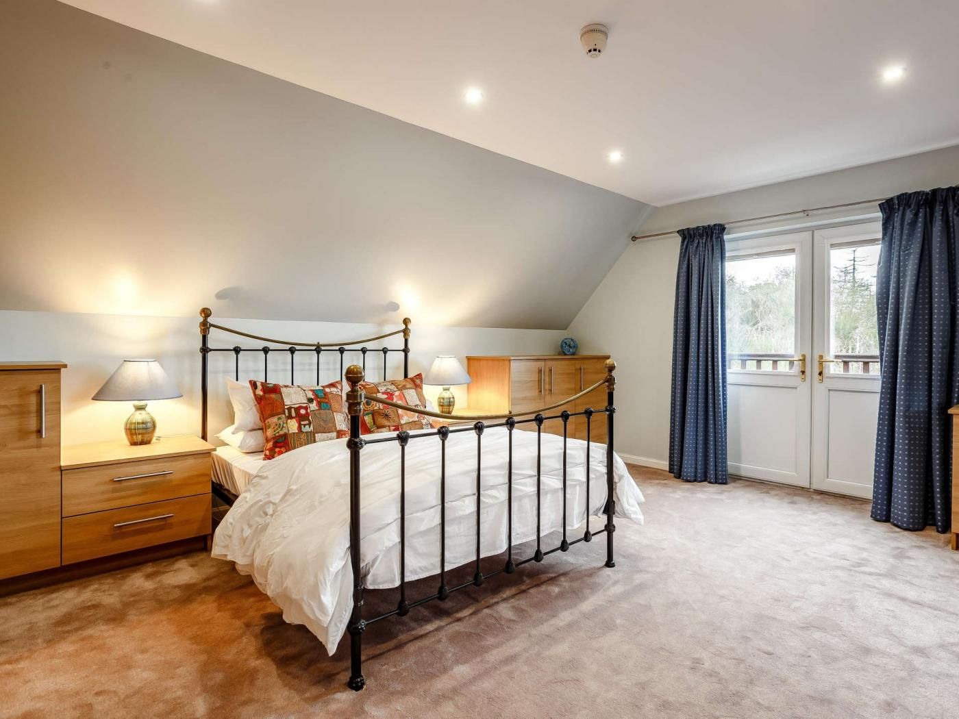 Une chambre à coucher comprenant un lit, des tables de chevet, une commode, une fenêtre avec des rideaux et un luminaire au plafond.