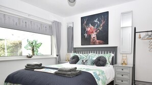 Un dormitorio con cama, mesita de noche, planta en maceta y un cuadro en la pared.