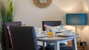Un comedor con una mesa redonda para dos, un espejo en la pared y una lámpara en una mesita auxiliar.