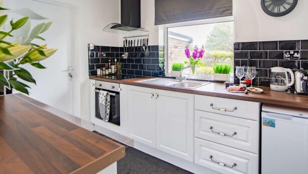 Una cocina moderna con armarios blancos, protector contra salpicaduras negro y una ventana con vistas a zonas verdes.