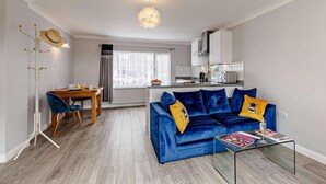 Een moderne woonkamer met een blauwe bank, een glazen salontafel, en een eethoek met een houten tafel en stoelen.